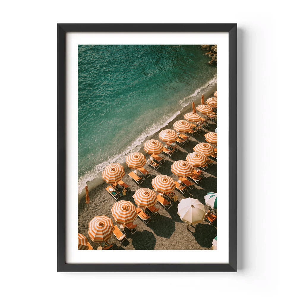 Framed artwork of a beach scene with orange umbrellas and lounge chairs.