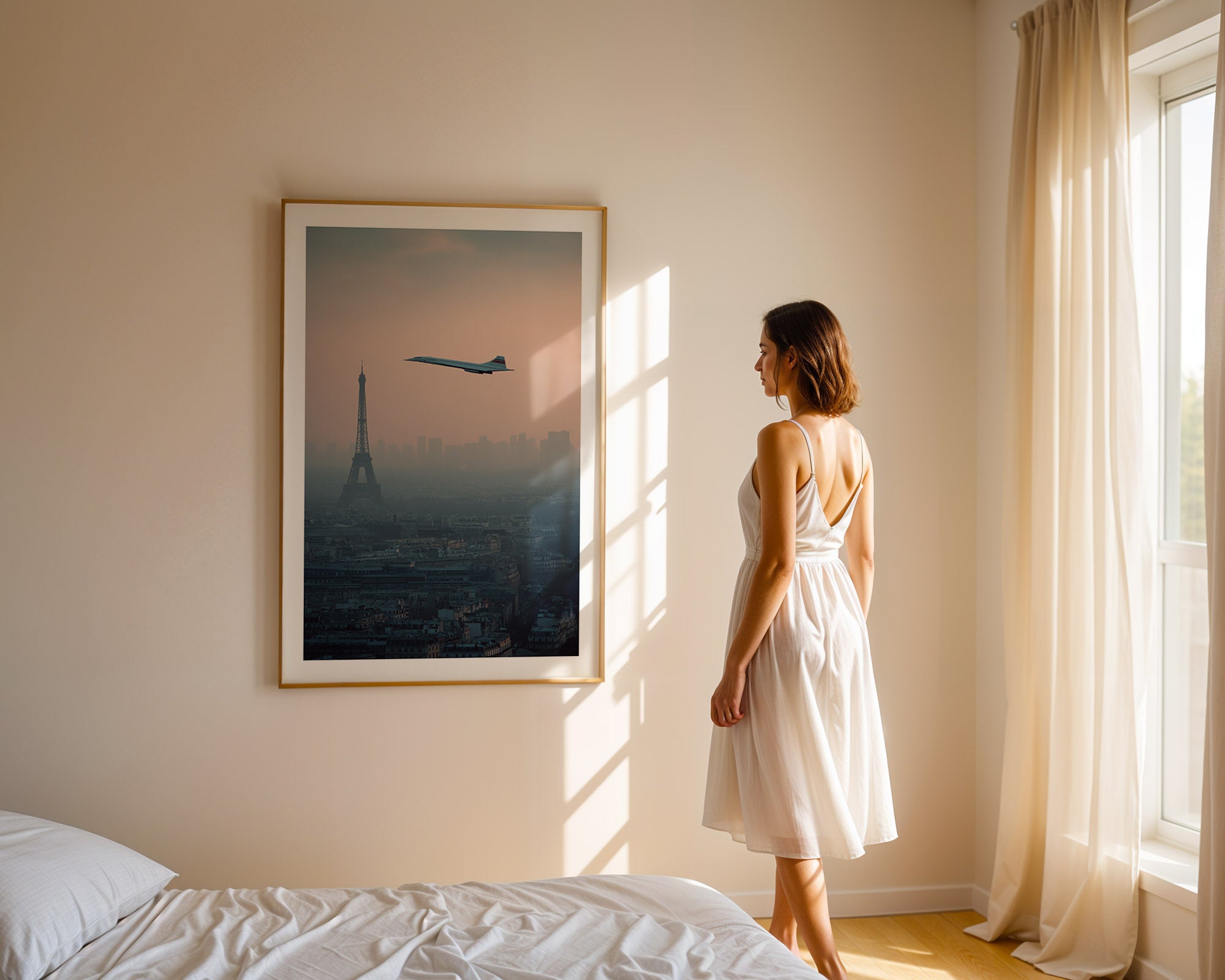 Woman in a white dress standing in a room with a large framed picture of the Eiffel Tower and an airplane.