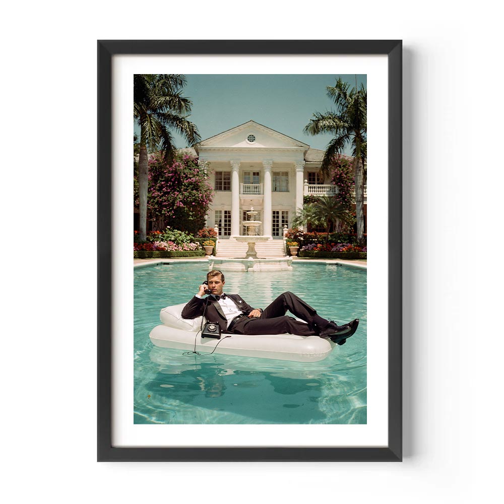 Man lounging on an inflatable pool float in a luxurious pool with a mansion in the background