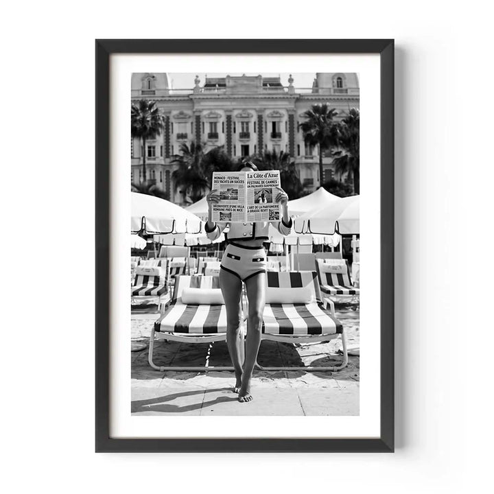 Person in a swimsuit standing on a beach with striped chairs and a building in the background