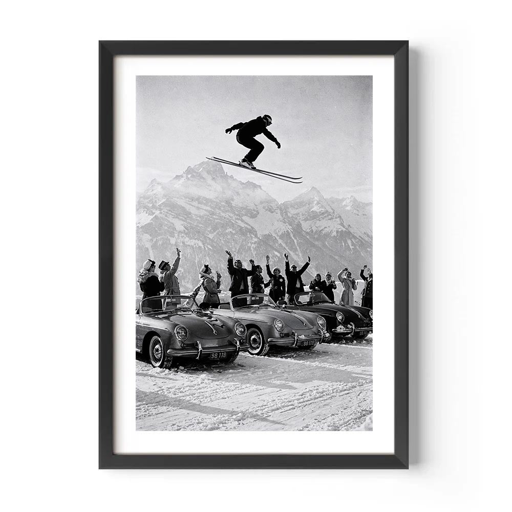Framed black and white print of a skier jumping over vintage cars with spectators in the snow.