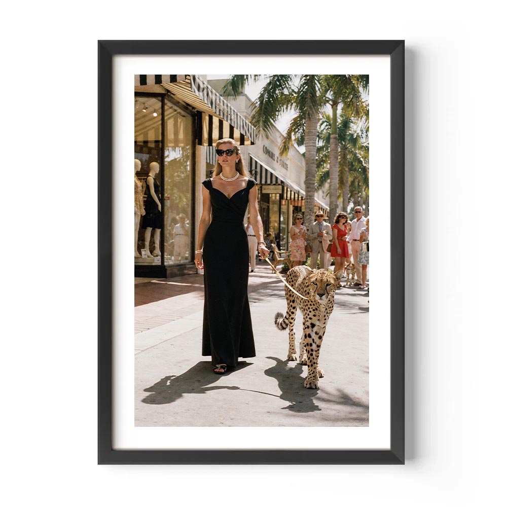 Framed photograph of a woman in a black dress walking a leopard on a city street.