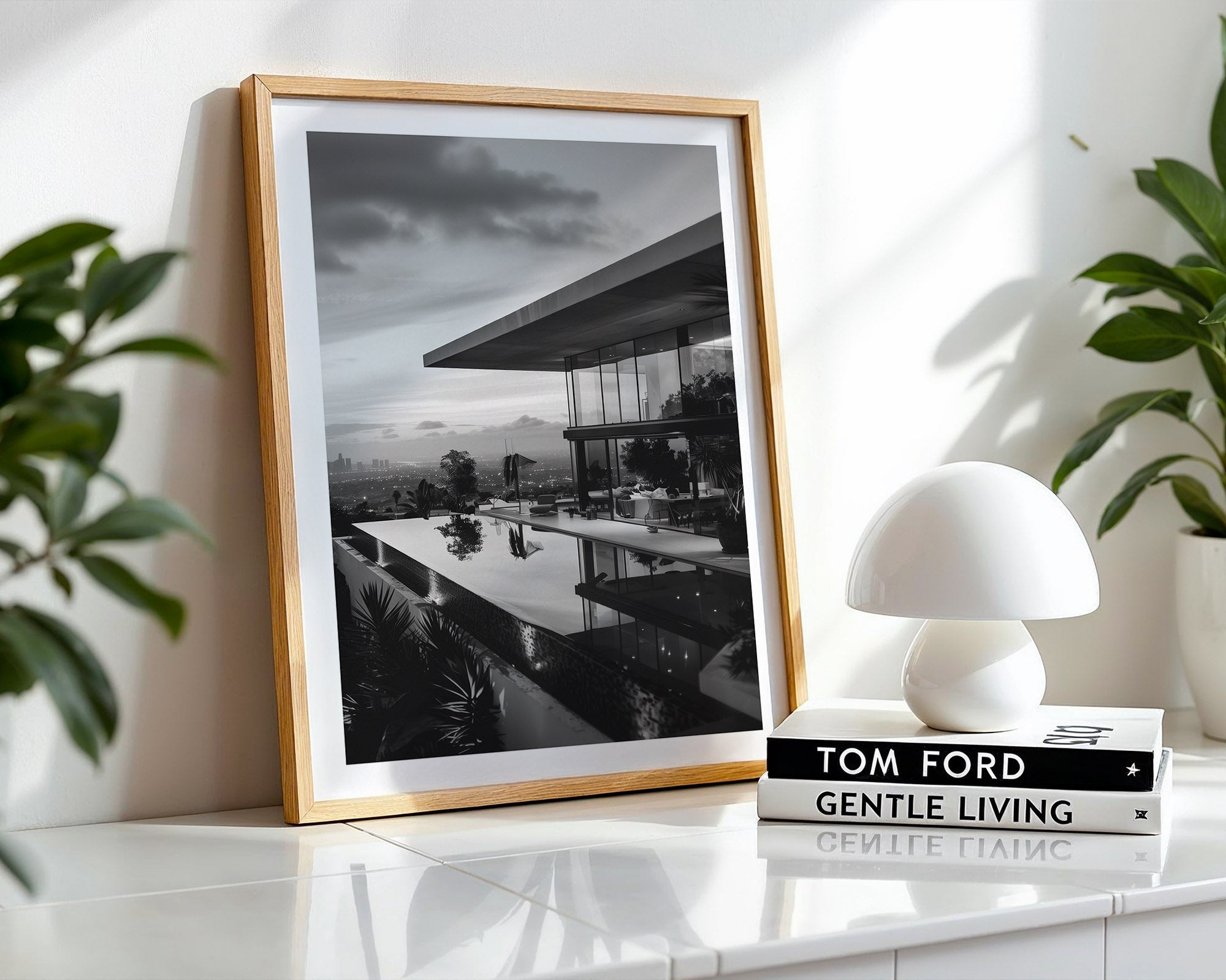 Framed black and white landscape print on a white surface with a white lamp and books.