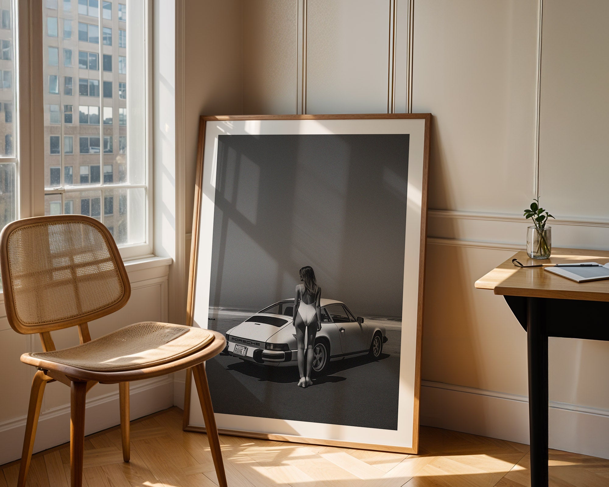 Framed photograph of a woman standing next to a car in a room with a chair and table.