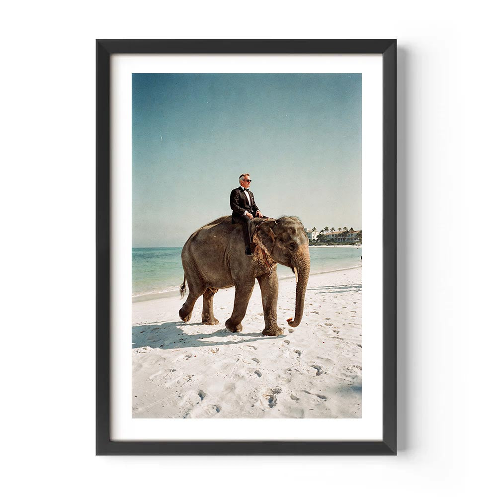 Framed photograph of a man riding an elephant on a beach.