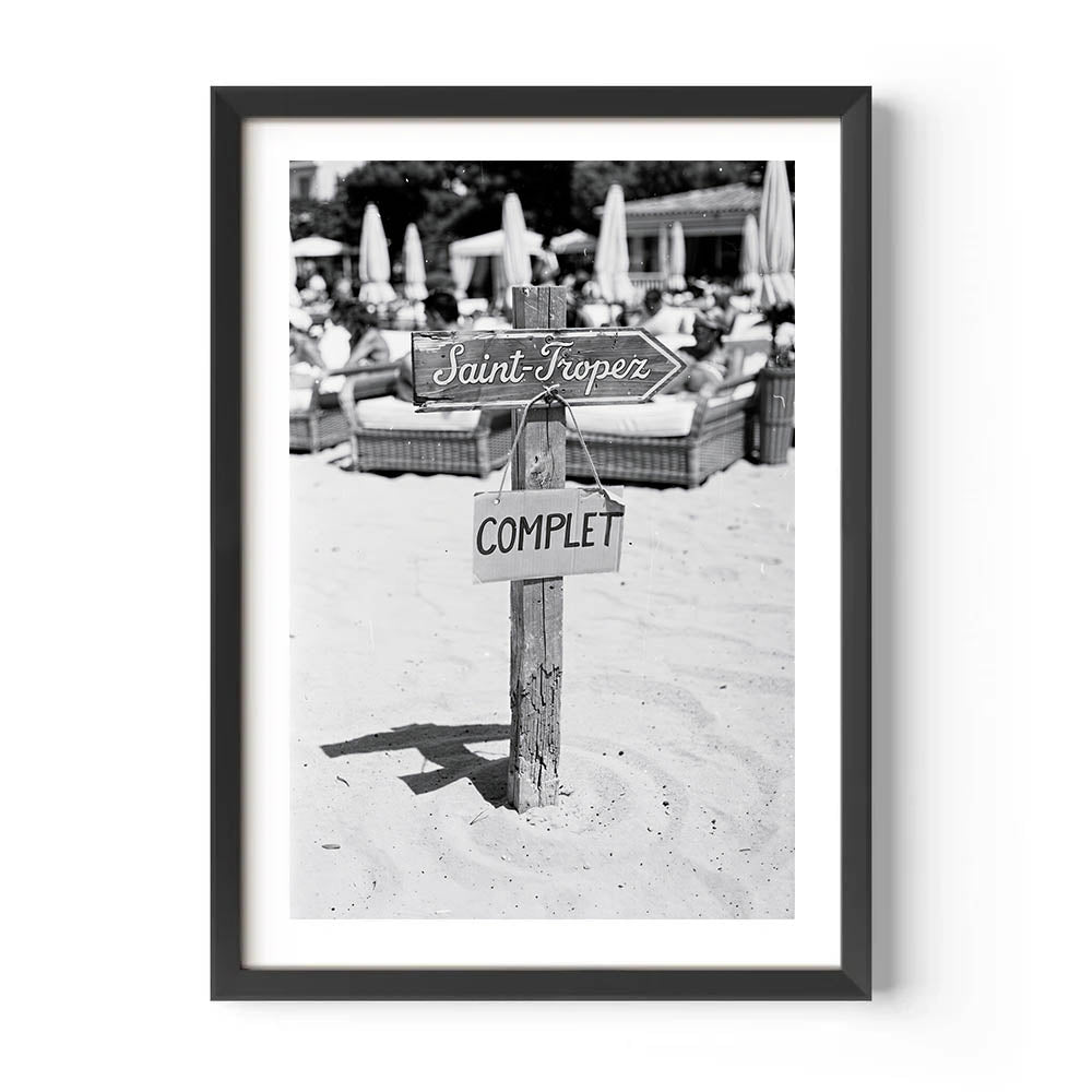 Framed black and white photo of a beach scene with signs on a post.