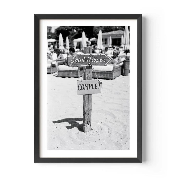 Framed black and white photo of a beach scene with signs on a post.