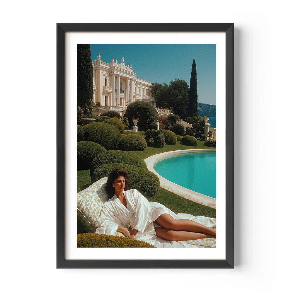 Framed photograph of a woman in a white robe lying on a grassy area with a pool and classical building in the background.