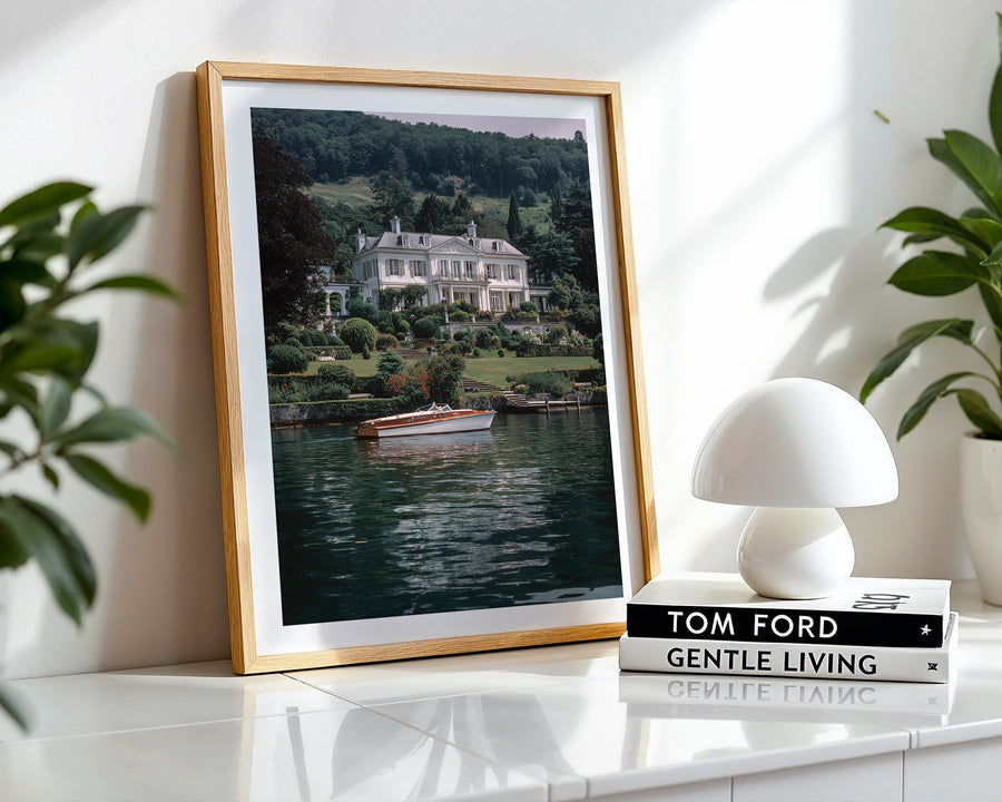 Framed photograph of a house by a lake on a white surface with a white lamp and books.
