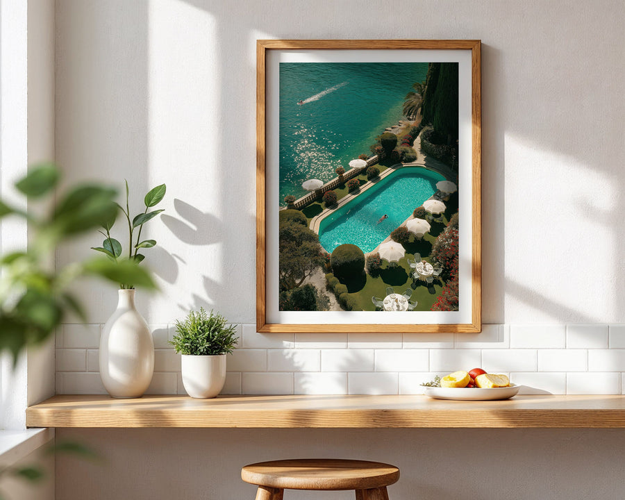 Framed artwork of a pool scene on a wall with a wooden shelf below.