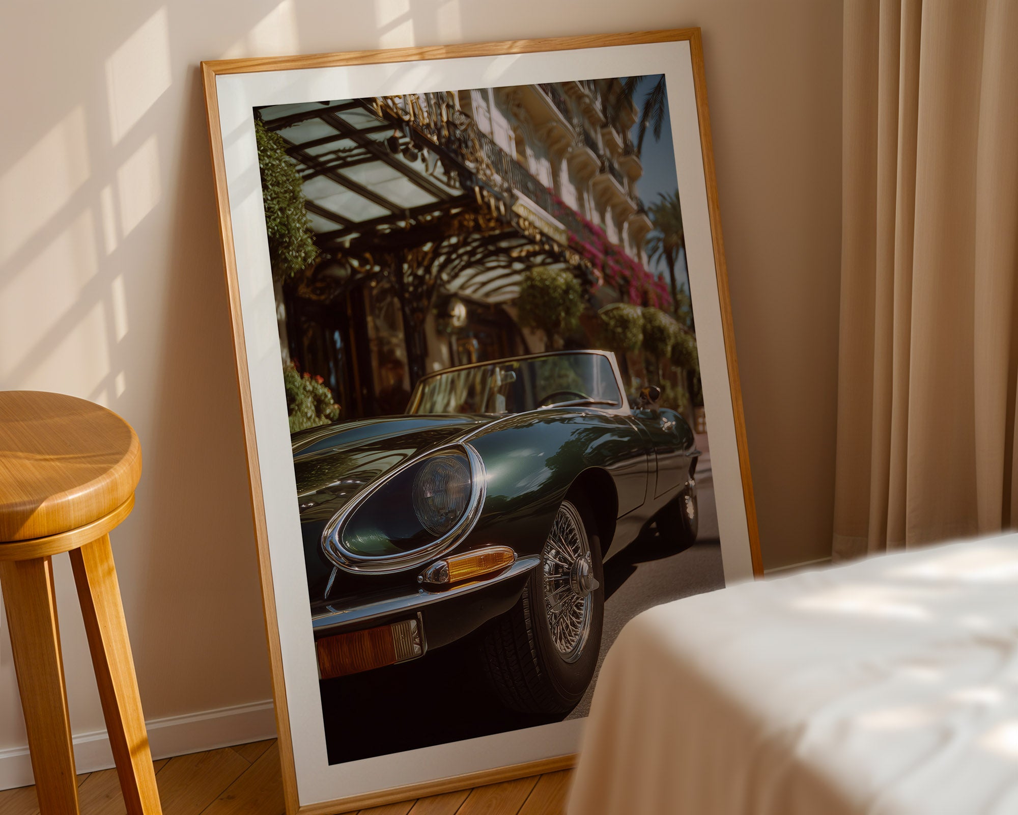 Framed photograph of a classic Jaguar e-type on a wall next to a wooden stool and bed.