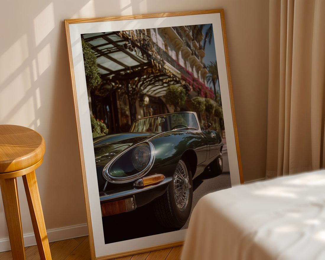 Framed photograph of a classic Jaguar e-type on a wall next to a wooden stool and bed.