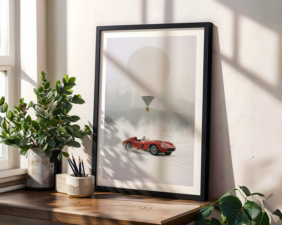 Framed artwork of a red car and hot air balloon on a wall with plants and a window.