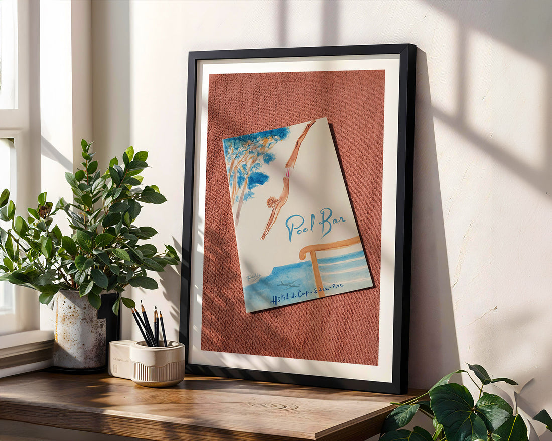 Framed artwork on a wooden shelf with plants. Hôtel du Cap-Eden-Roc