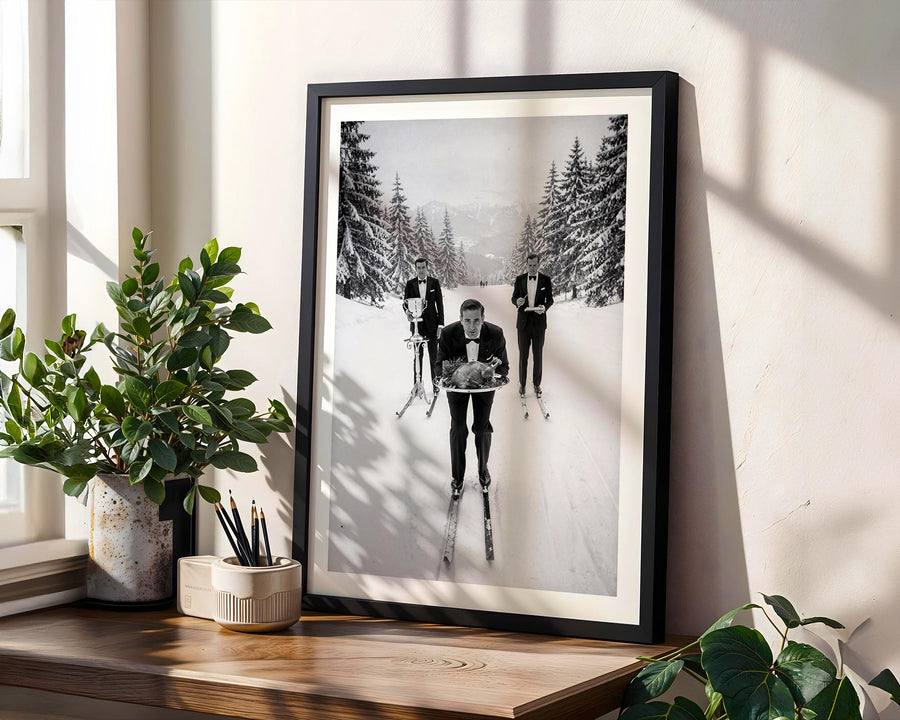 Framed black and white photograph of people skiing in a snowy landscape on a wooden shelf with plants.