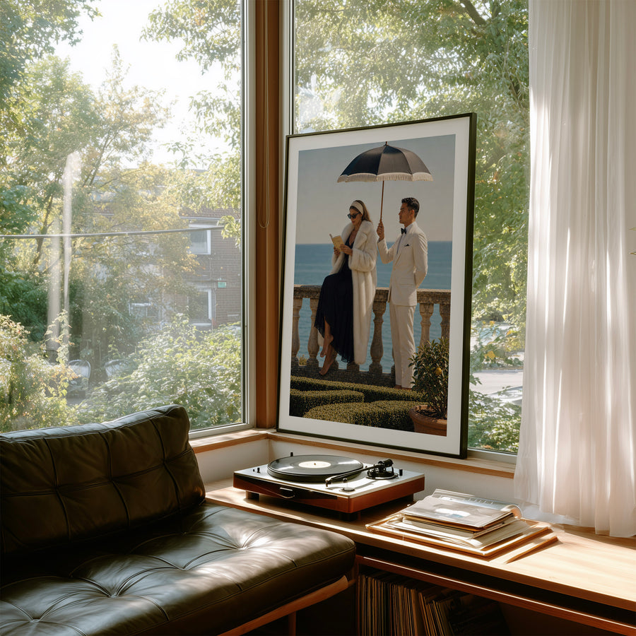 A large framed art print featuring a vintage photograph of a couple under an umbrella by the sea, displayed on a wooden window sill in a modern living room setting with a leather sofa and a turntable.