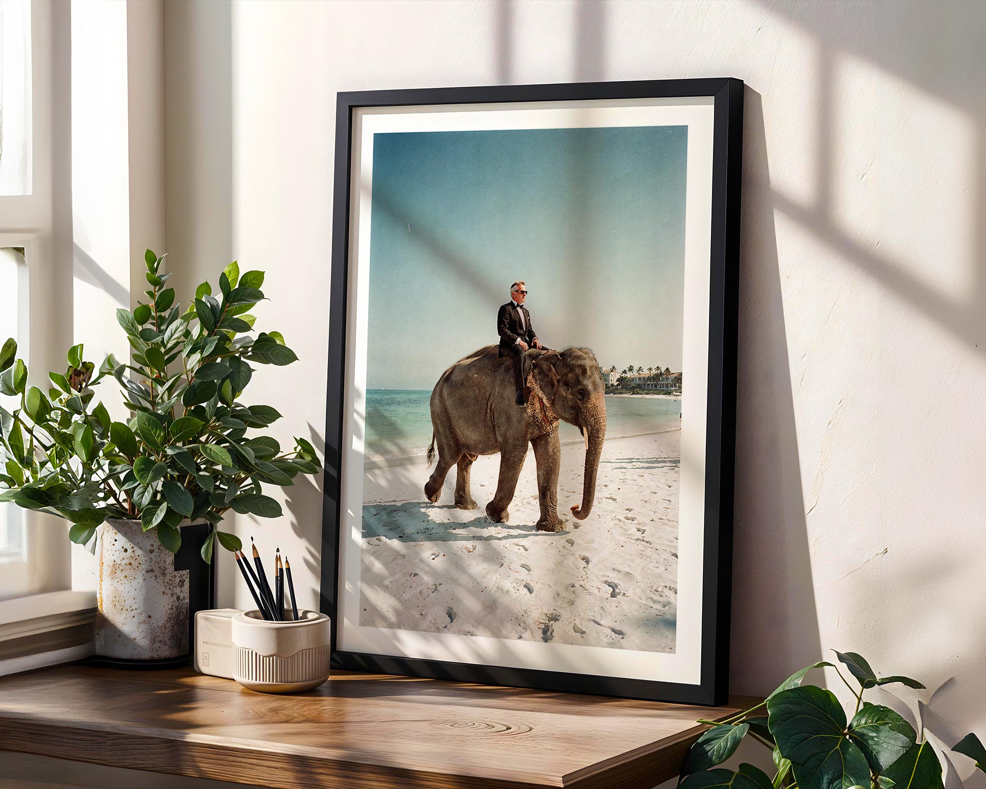 Framed photograph of a person riding an elephant on a beach, placed on a wooden shelf with plants.