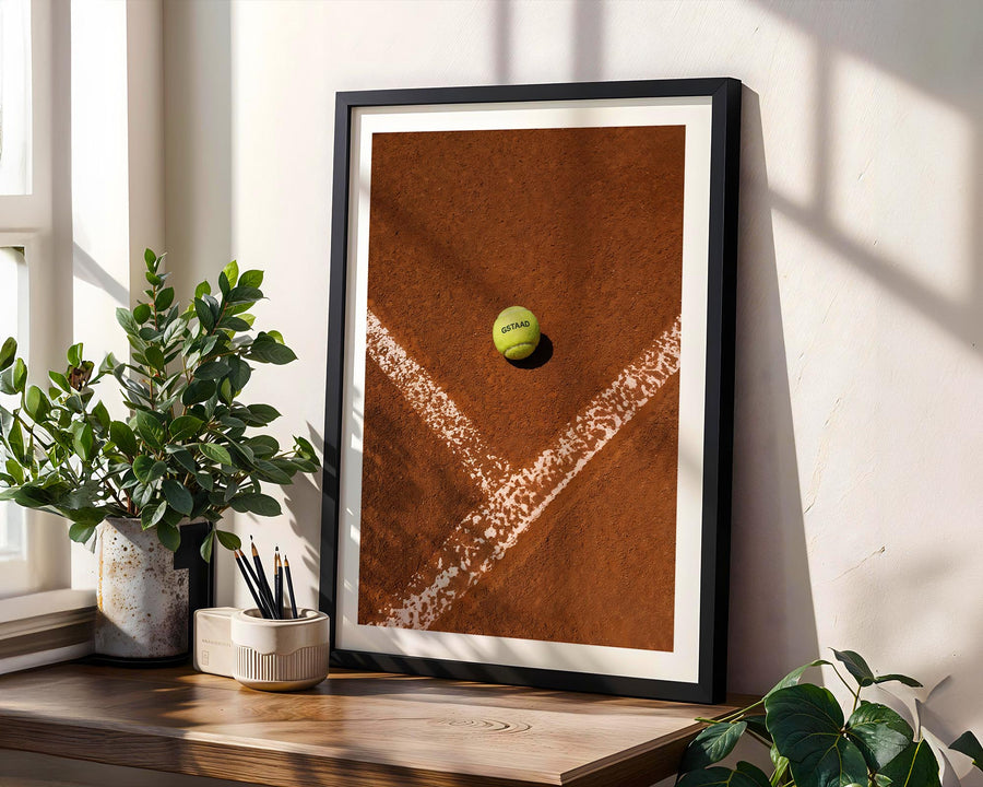 Framed artwork of a tennis ball on a court with plants and decor on a windowsill.