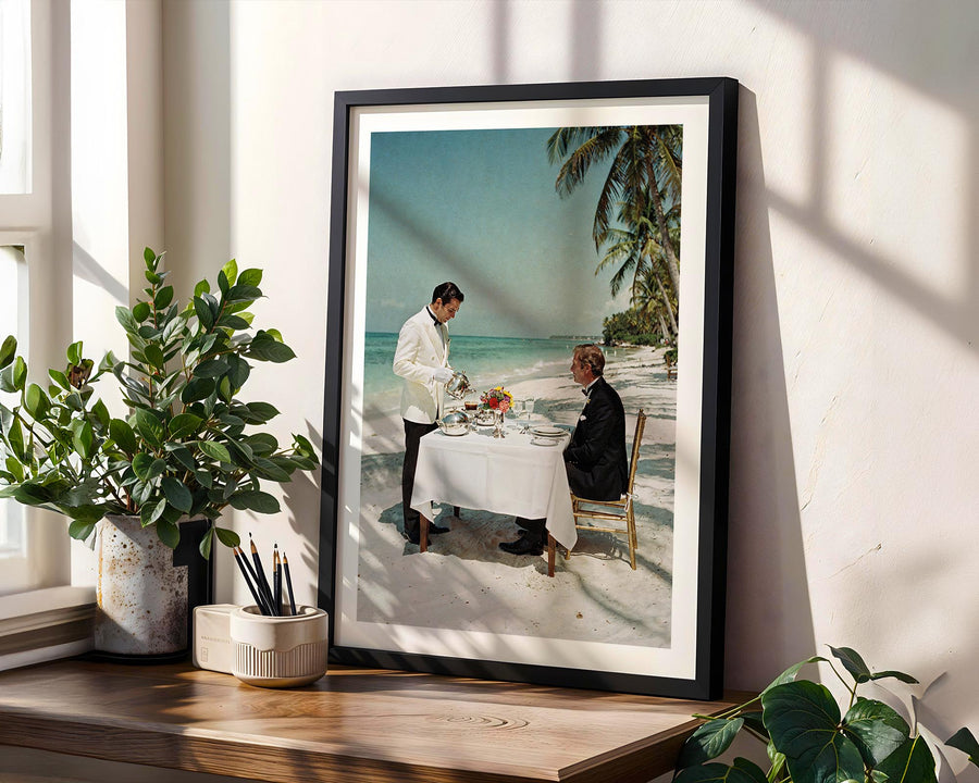 Framed photograph of a couple dining on a beach with indoor plants and decor.