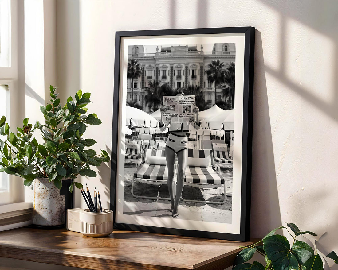 Framed black and white print of a person on a beach with palm trees, placed on a wooden shelf.