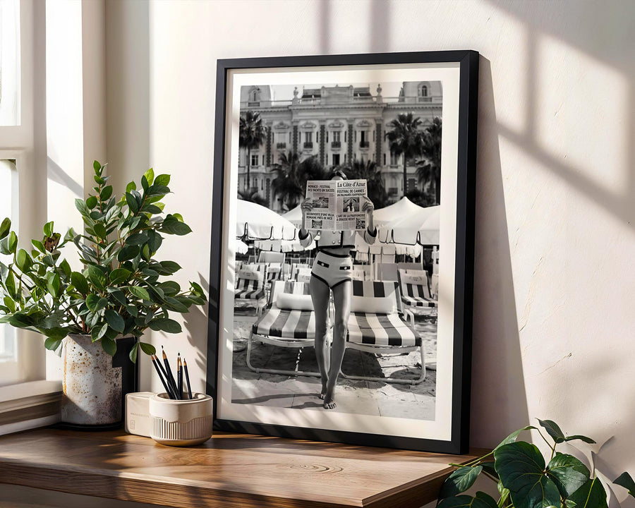 Framed black and white print of a person on a beach with palm trees, placed on a wooden shelf.