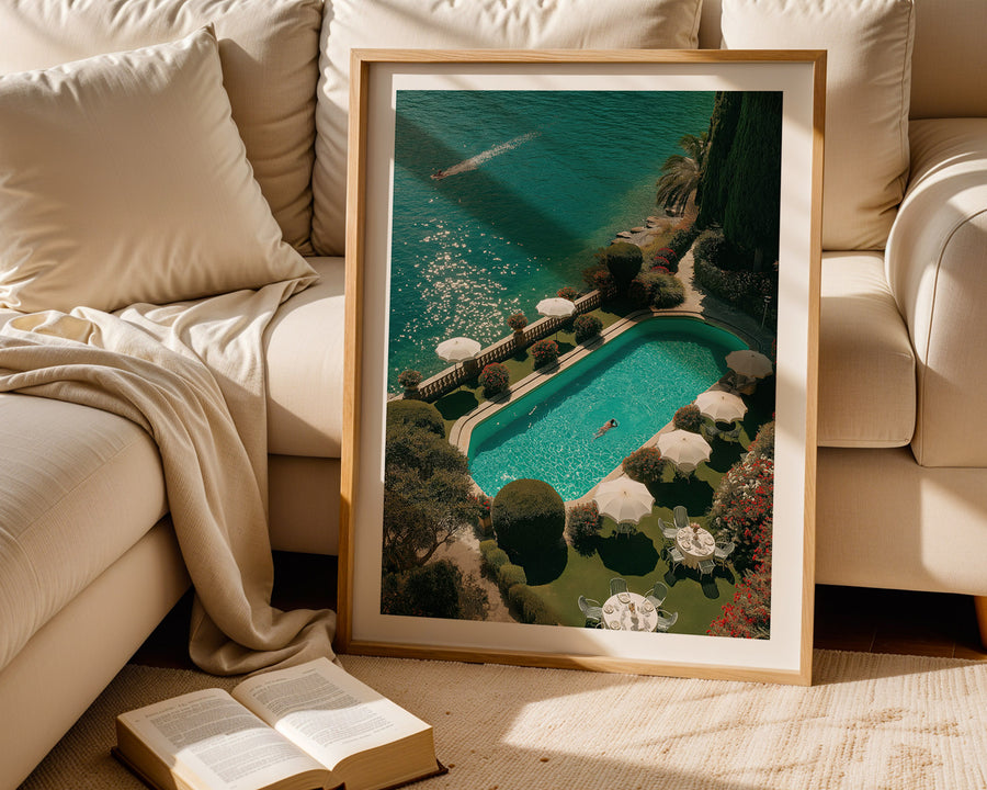 Framed artwork of a pool scene on a beige sofa with an open book.
