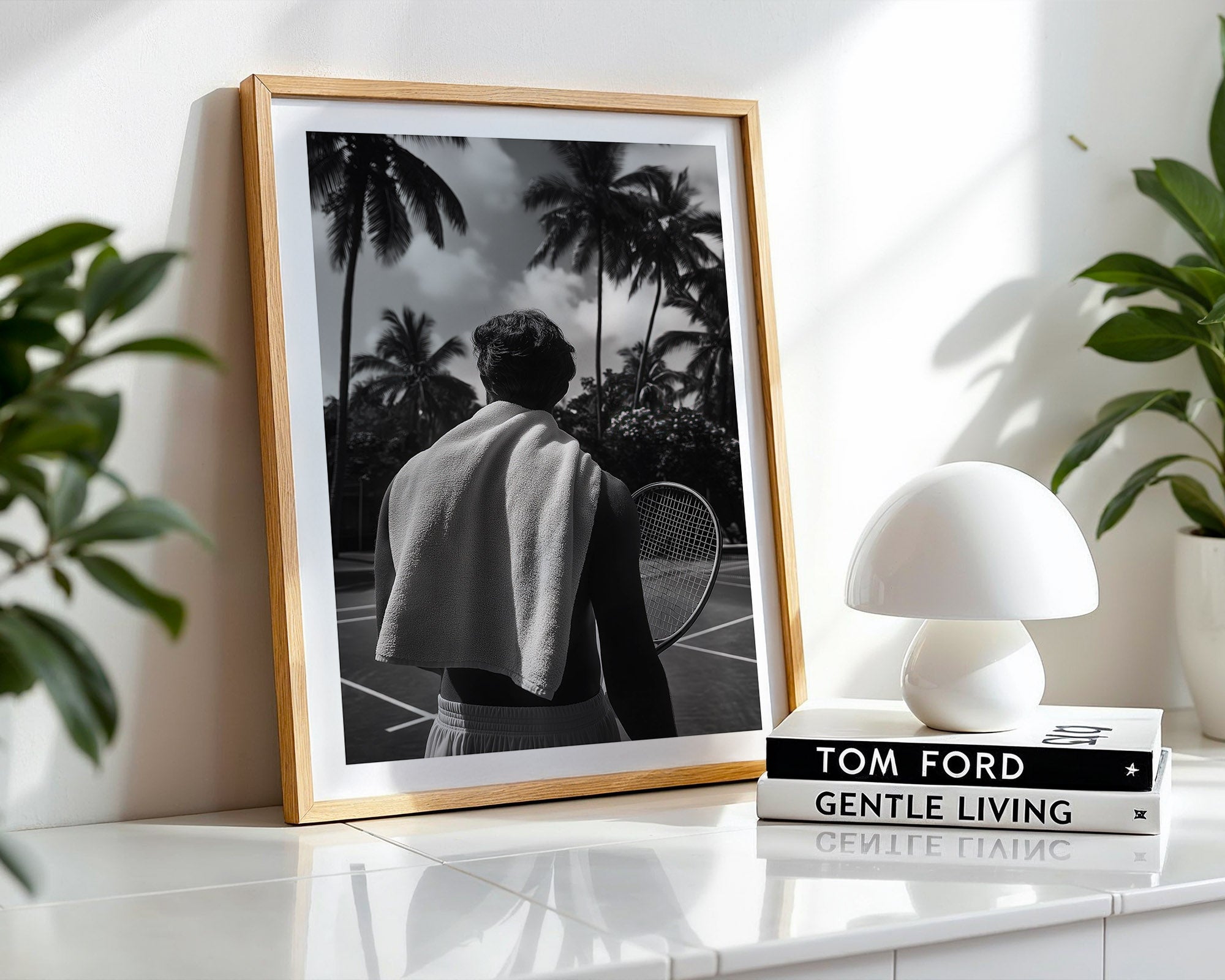 Framed black and white photo of a person with palm trees, placed on a shelf with a lamp and books.