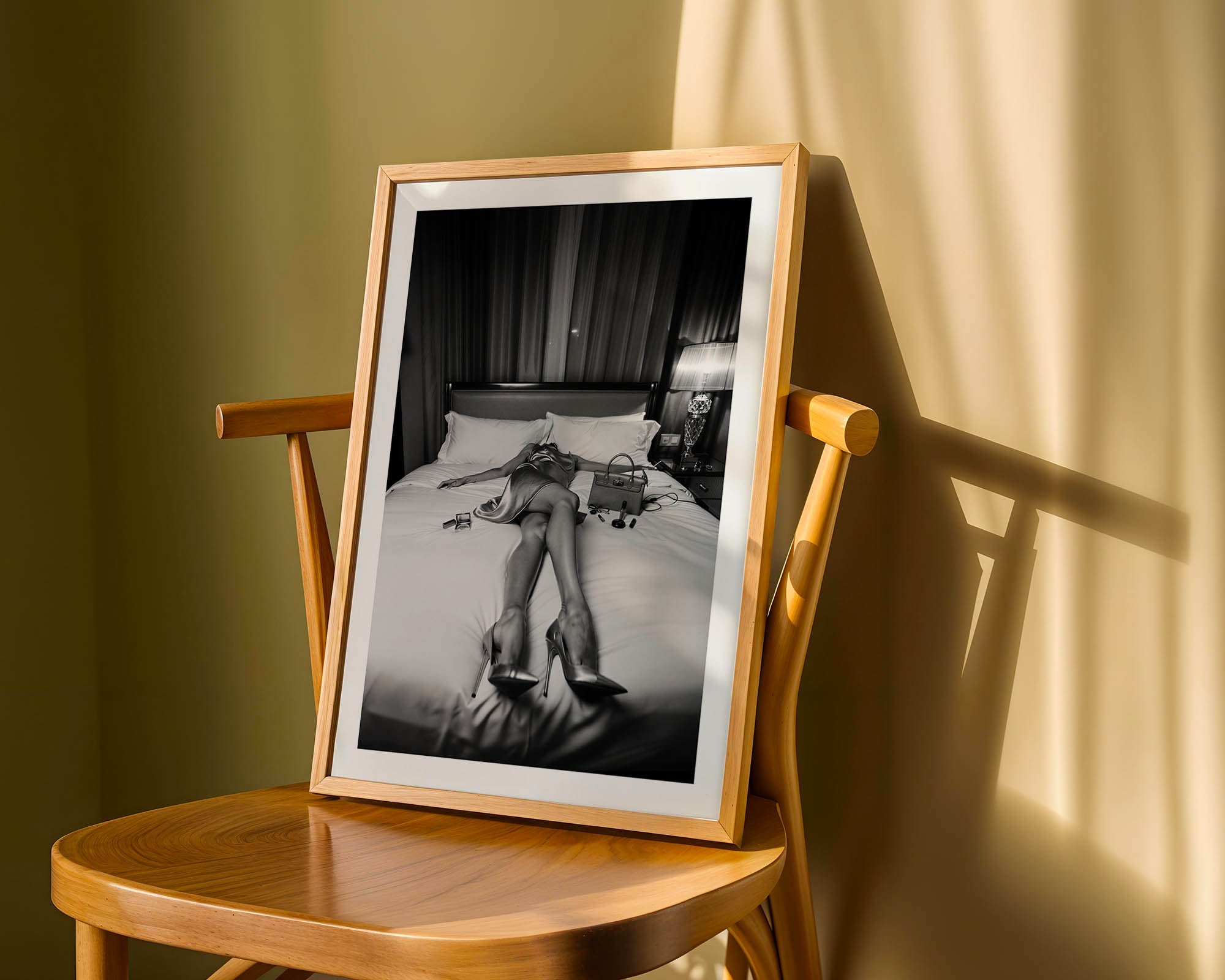 Framed black and white photograph of a person lying on a bed in a wooden frame, placed on a wooden chair.