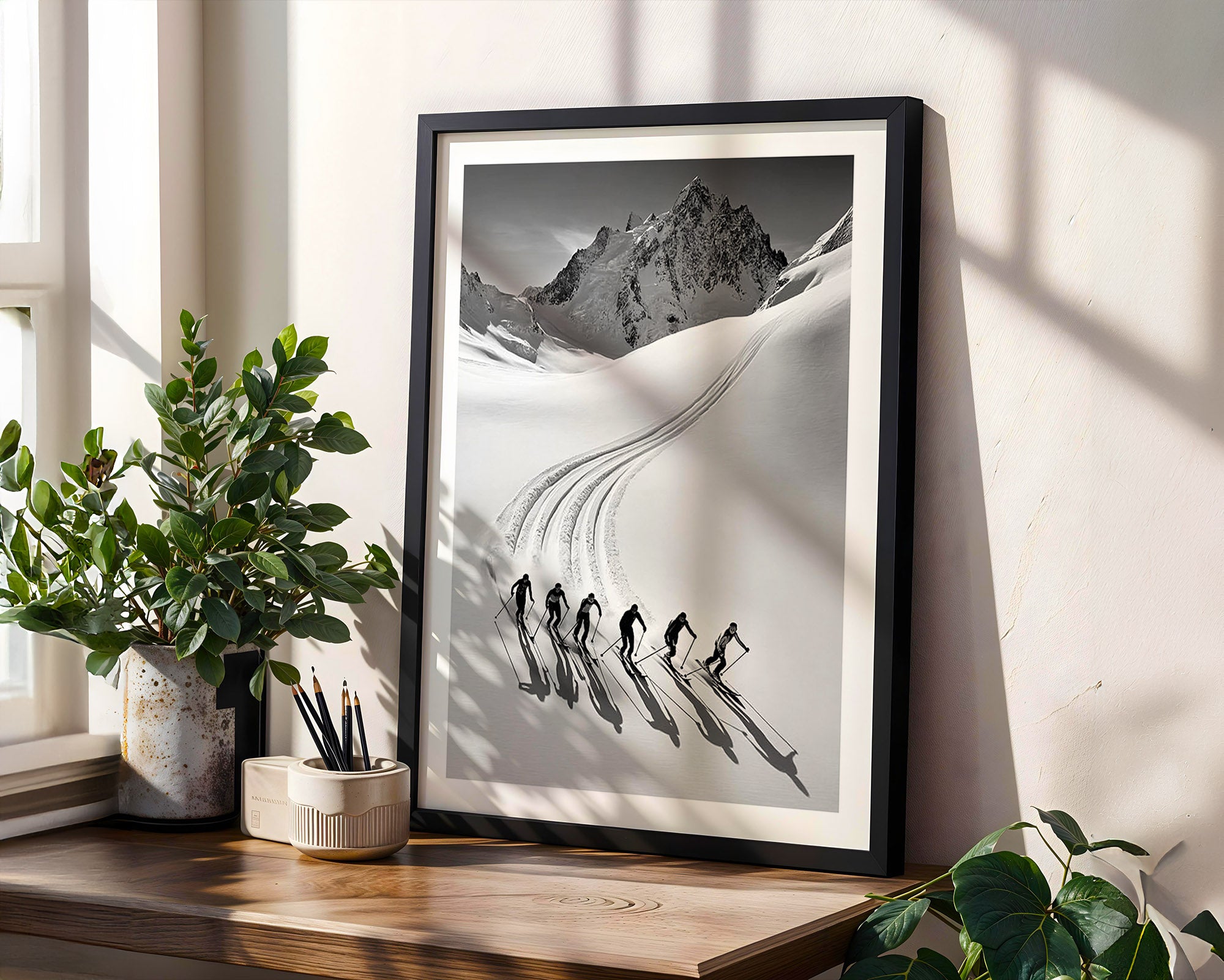 Framed black and white mountain print on a wall with plants and a window.