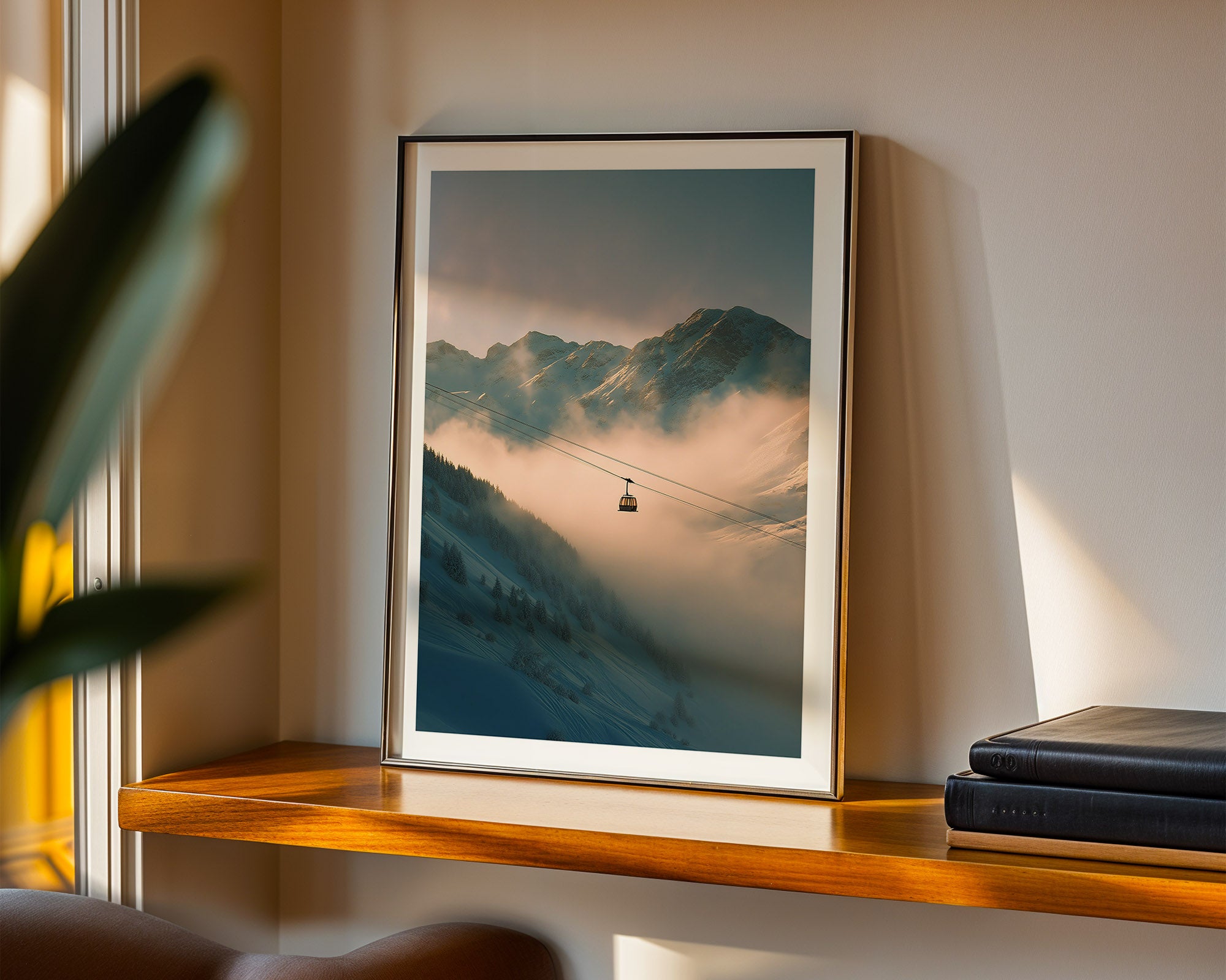 Framed mountain landscape print on a shelf with books and a plant.