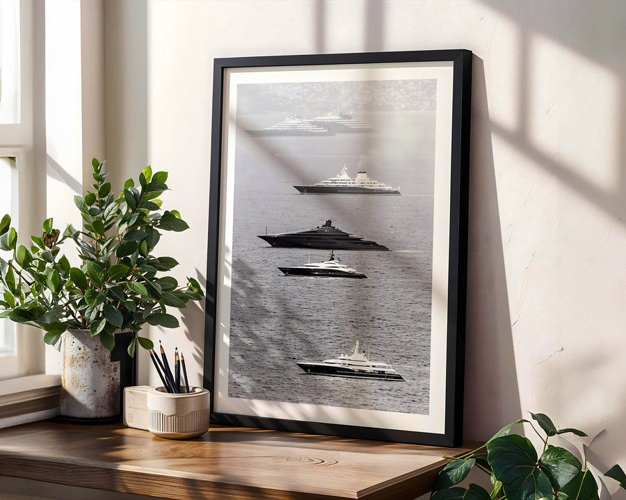 Framed artwork of ships on a wall with plants and a window in the background