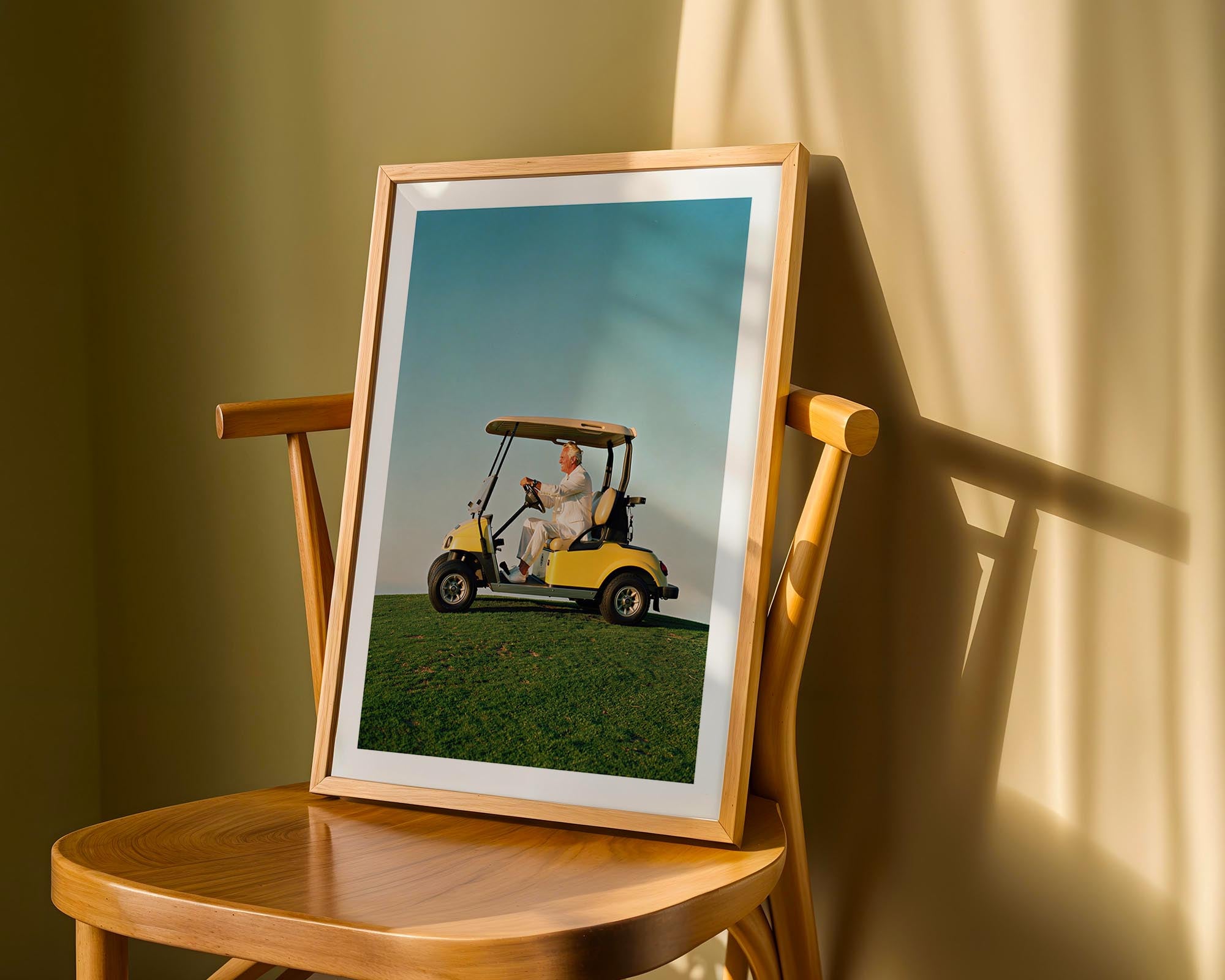 Framed picture of a person in a golf cart on a grassy field, displayed on a wooden chair.