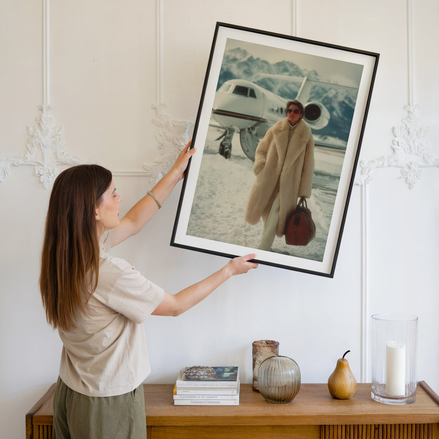 Woman hanging a framed photograph of a person in a coat near an airplane.