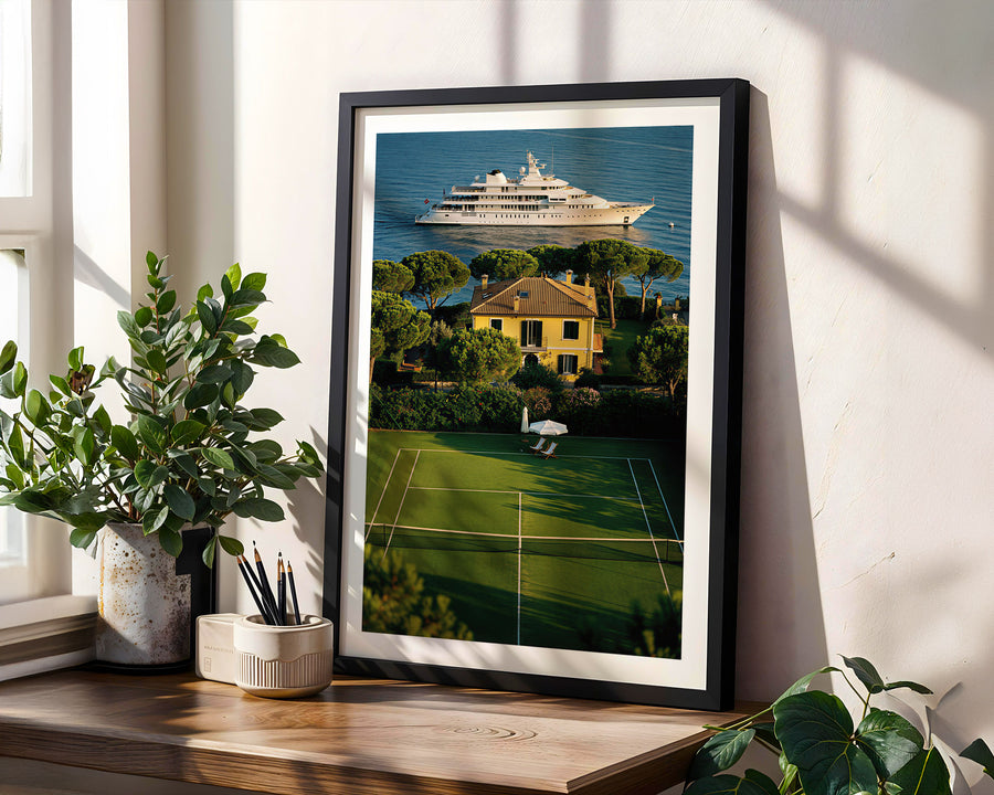 Framed artwork of a tennis court with a yacht on a wall in a bright room.