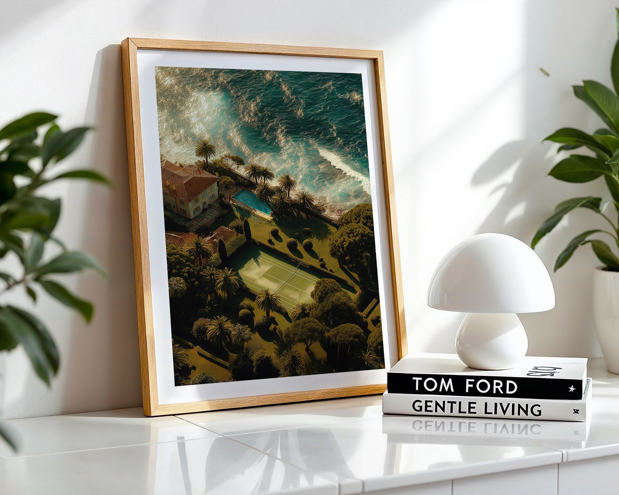 Framed artwork on a shelf with a white lamp and books in the background