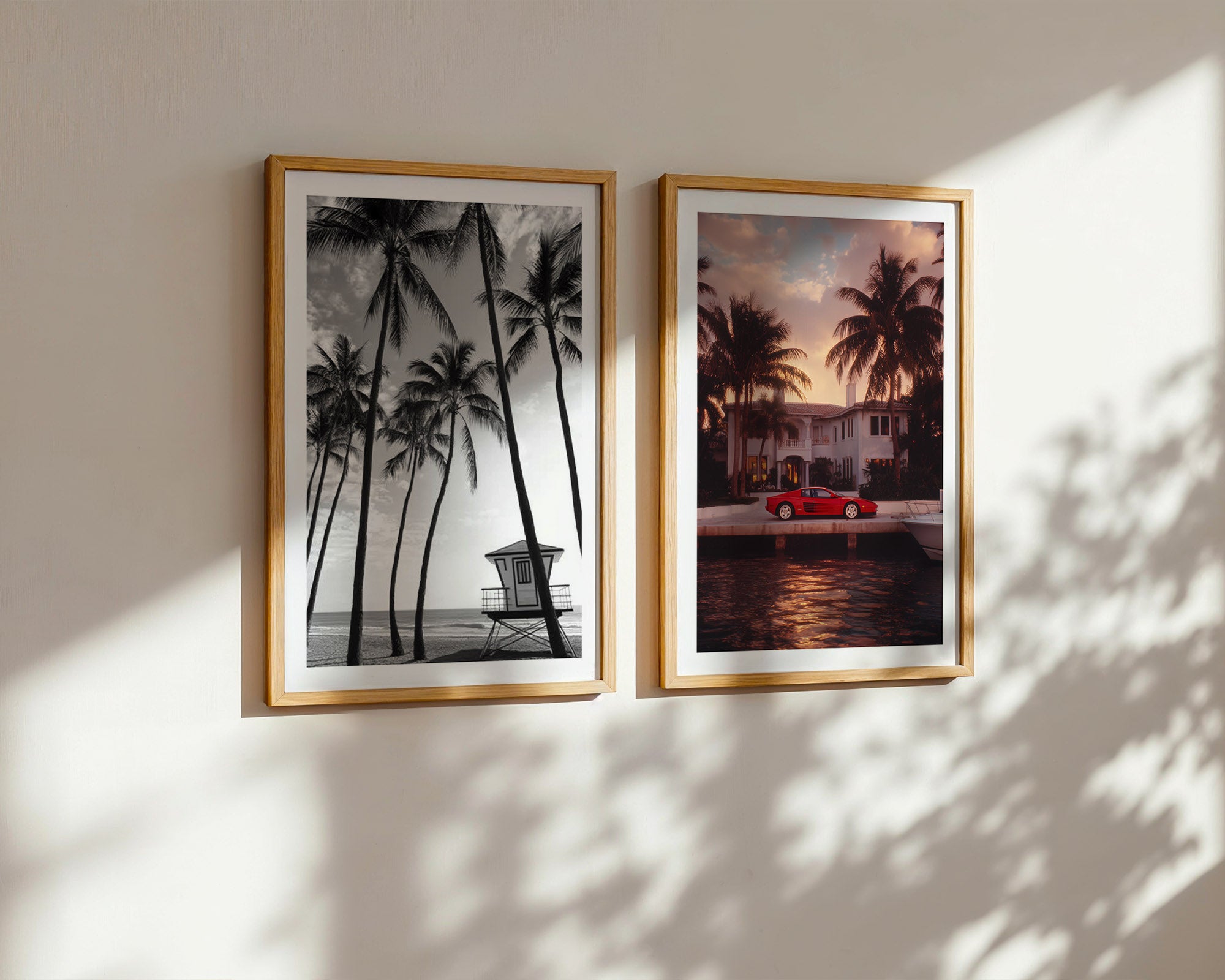Two framed artworks of tropical scenes on a wall with sunlight casting shadows.