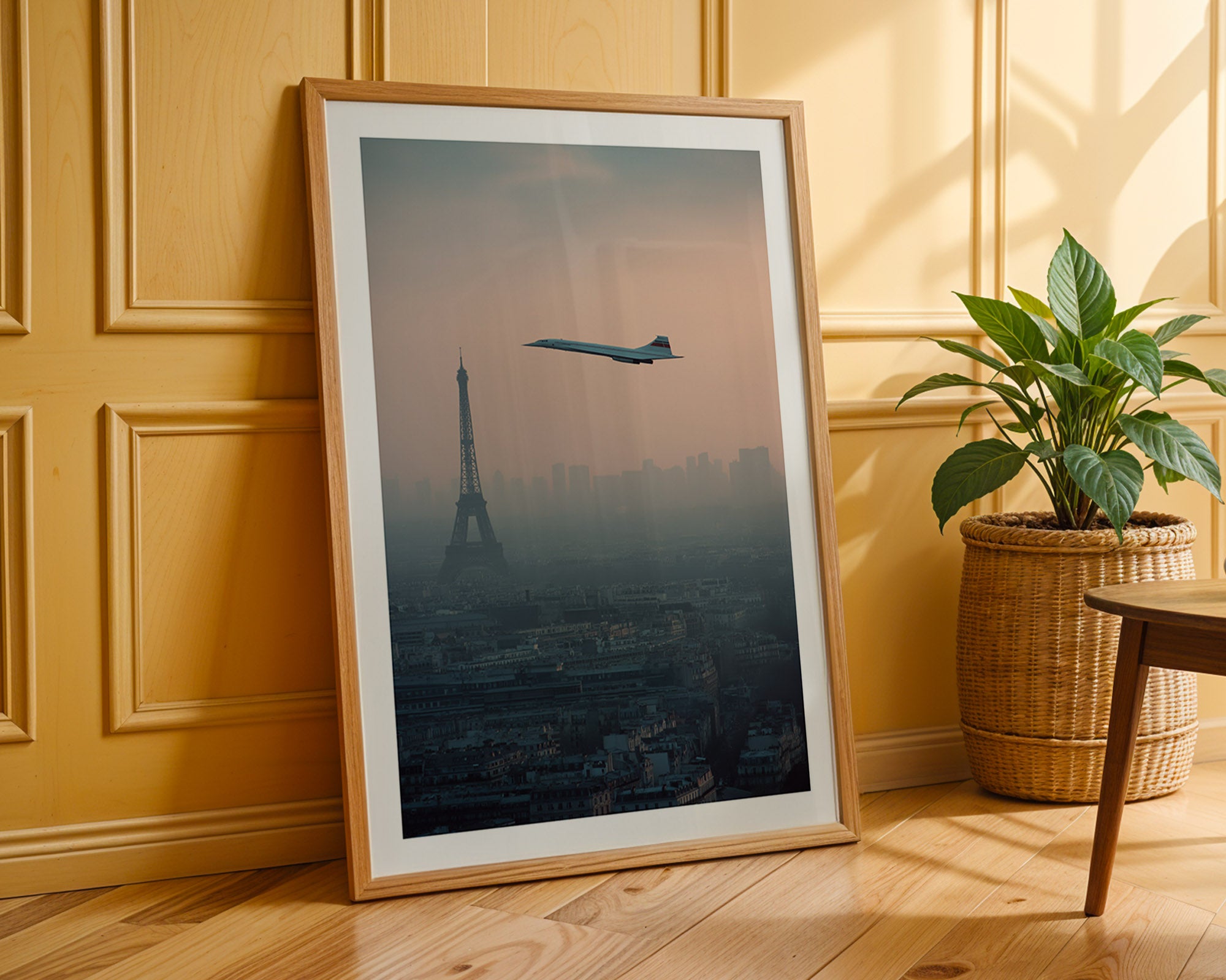 Framed artwork of an airplane over a cityscape with the Eiffel Tower, placed on a wooden floor against a wall.