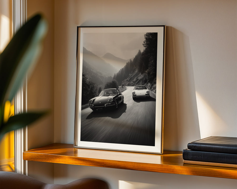 Framed black and white photograph of two Porsches on a mountain road on a wooden shelf.