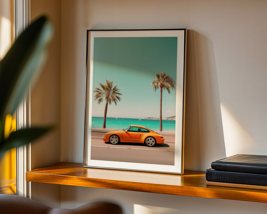Framed artwork of an orange sports car on a beach with palm trees.