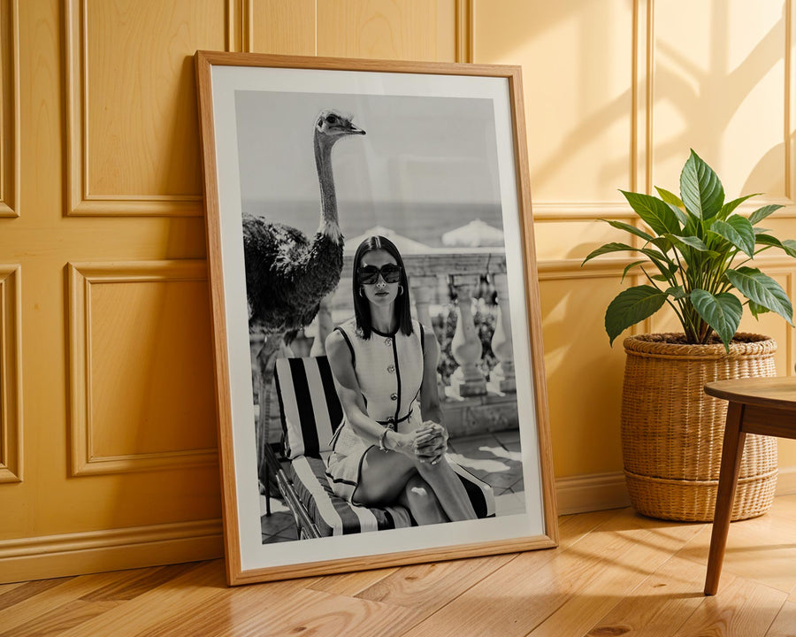 Framed black and white photo of a woman with an ostrich on a beach, leaning against a wooden wall.