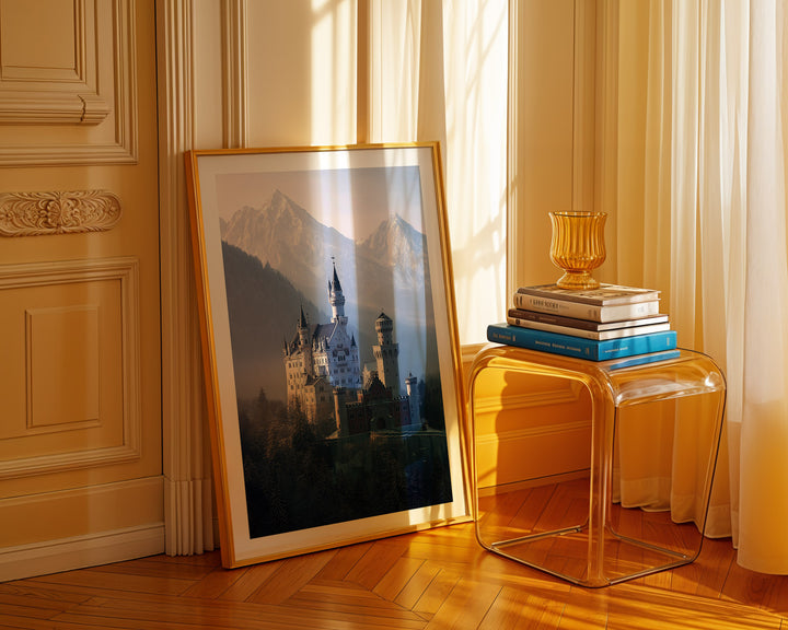 Framed picture of a castle on a wall next to a transparent side table with books and a vase.