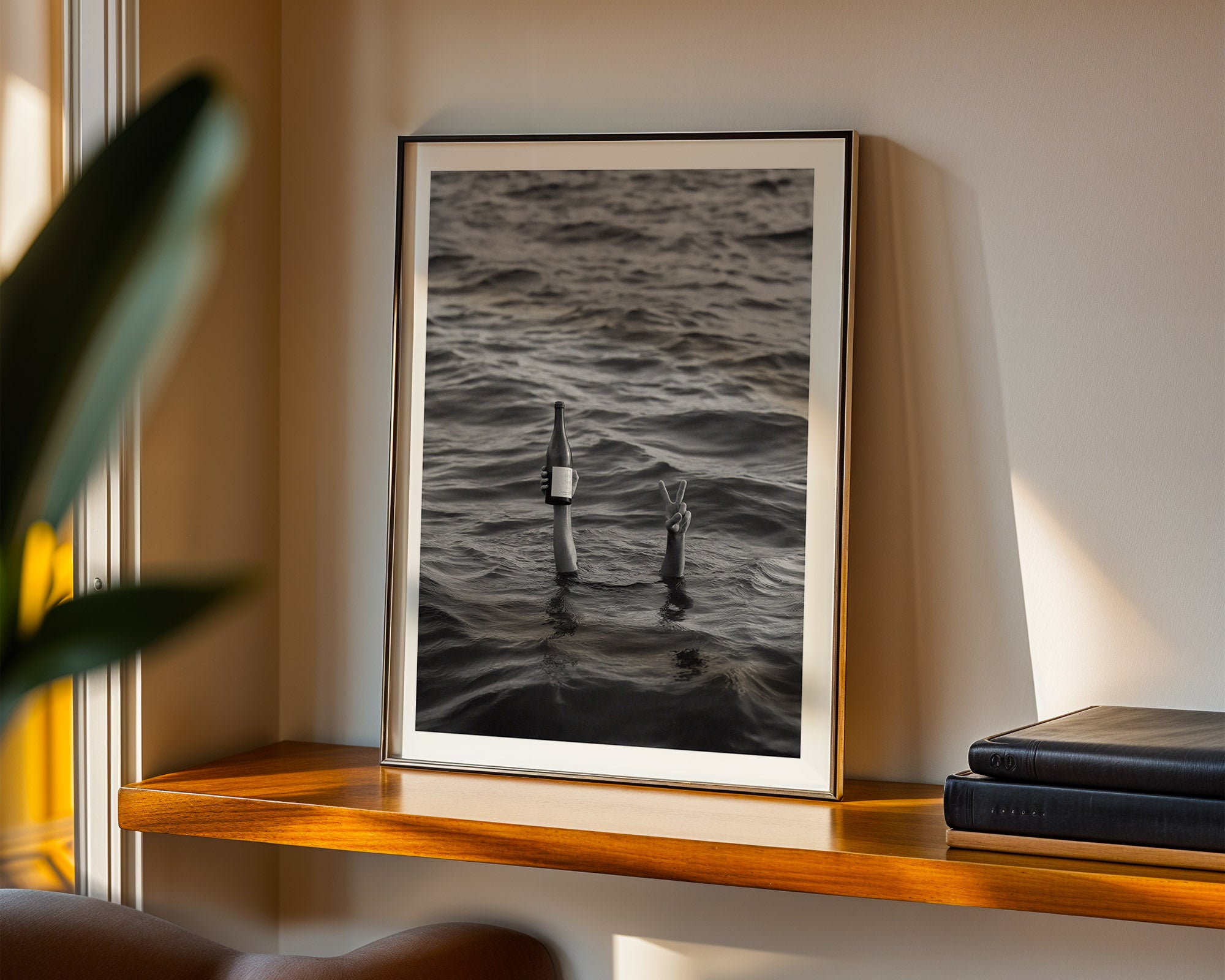 Framed artwork of a person and bottle in water on a shelf with books.