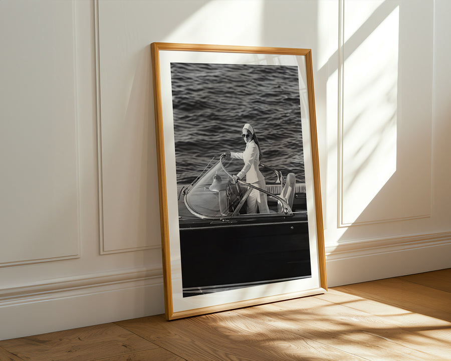 A framed black and white photograph leaning against a white paneled wall on a light wood floor, with warm sunlight casting shadows across the scene.