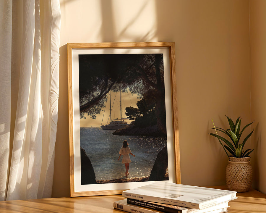 Framed artwork of a woman walking by a lake with a sailboat, placed on a shelf with books and a plant.