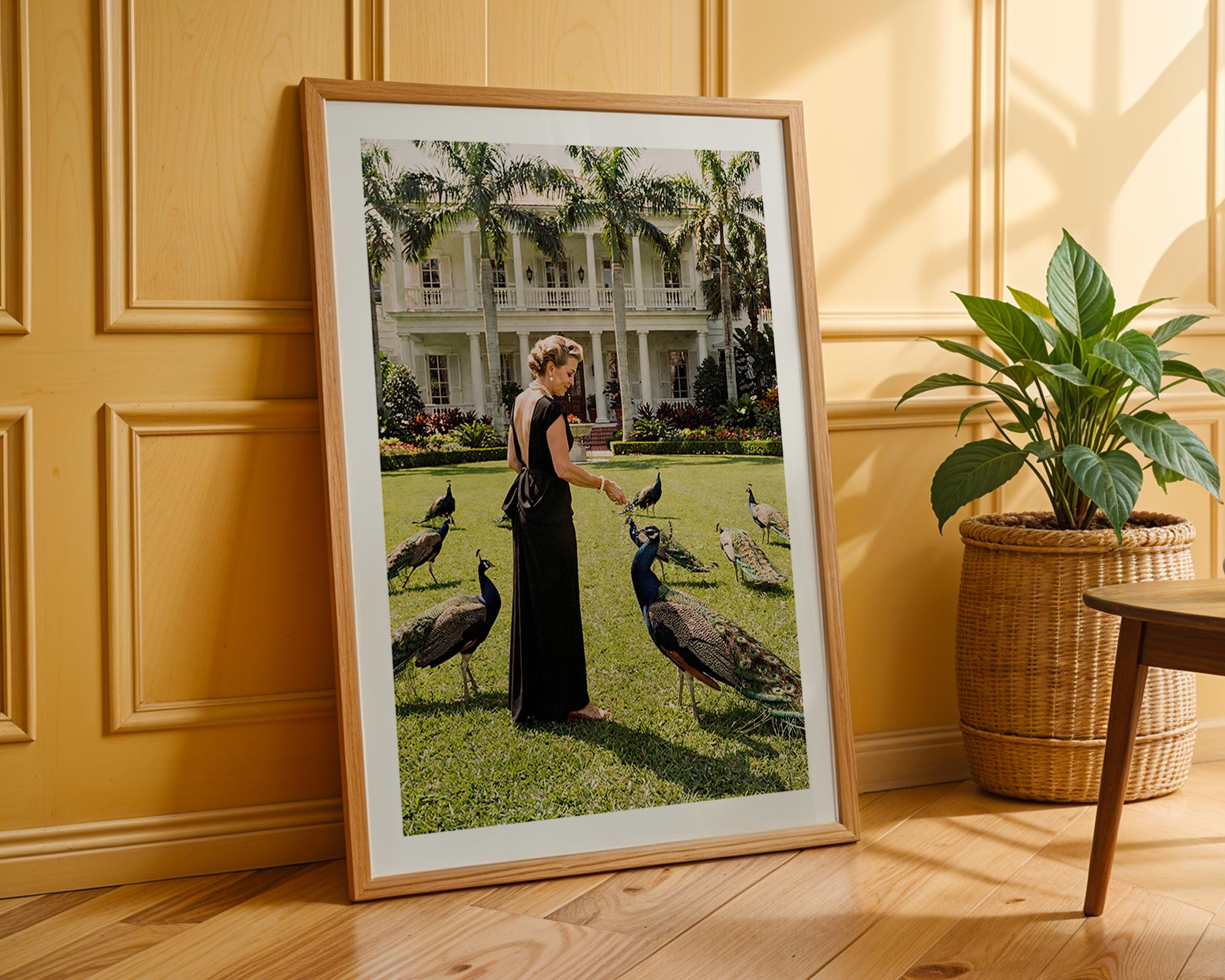 Framed photograph of a woman with peacocks in a garden setting, leaning against a wooden wall.