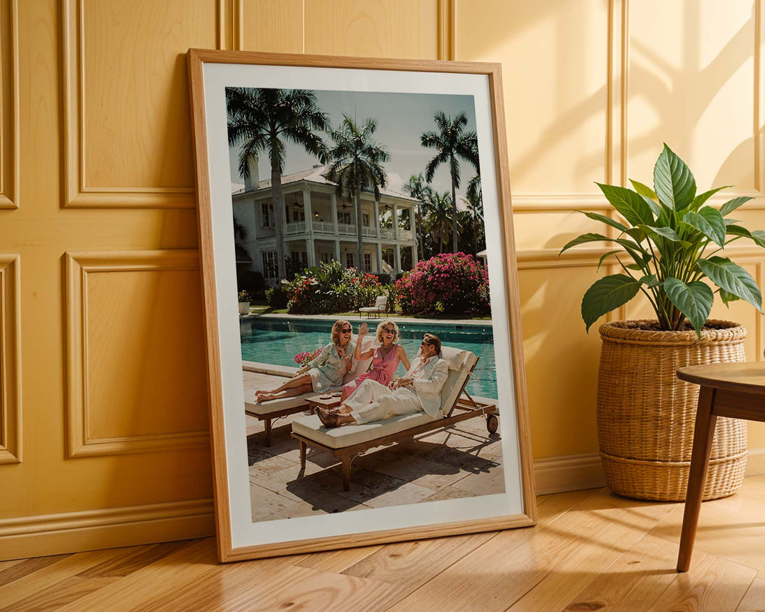 Framed photograph of a family by a pool with a house and palm trees in the background, leaning against a wooden wall.