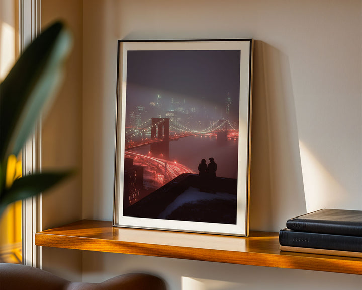 Framed artwork of a cityscape with a couple on a ledge, placed on a wooden shelf.