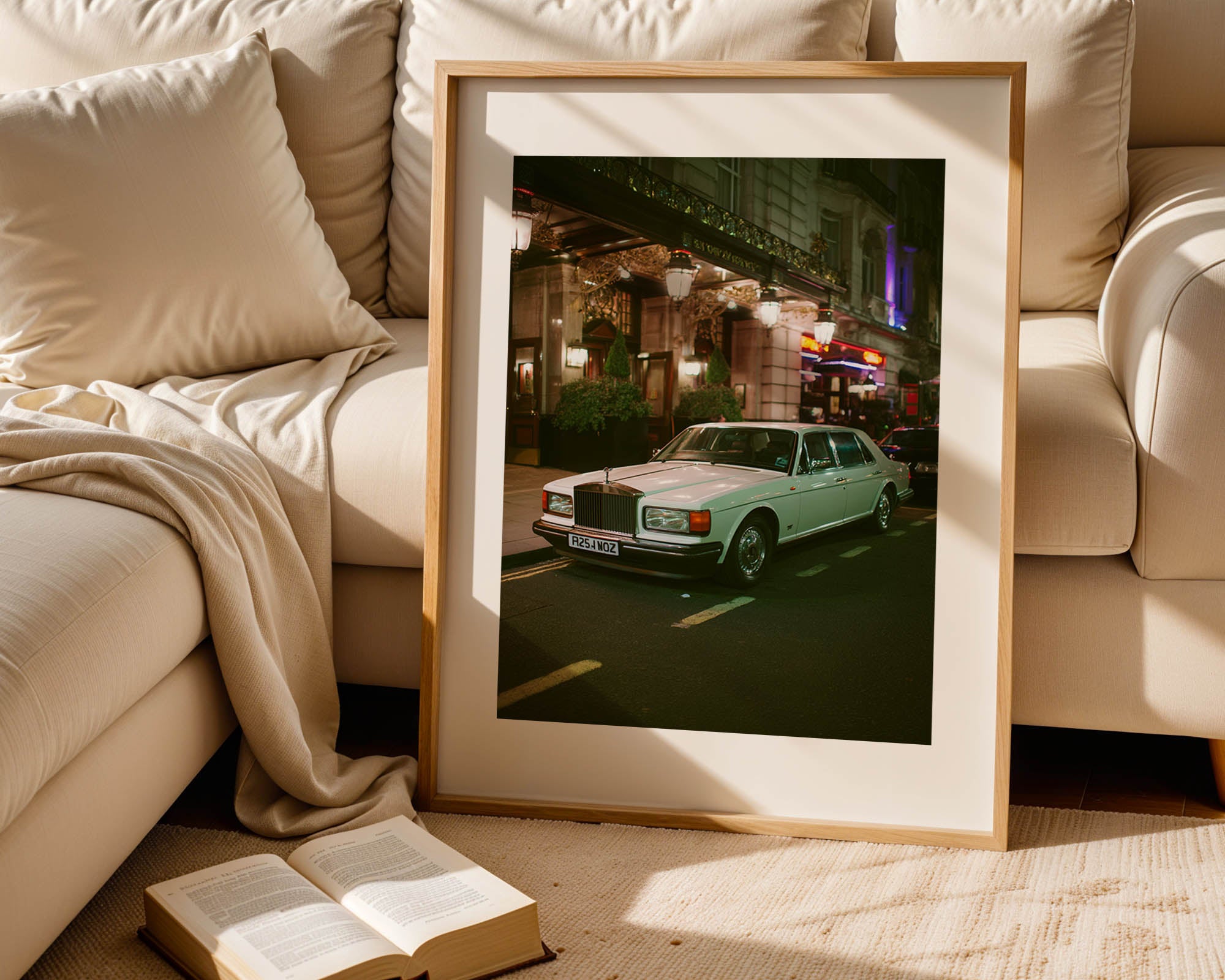 Framed photograph of a vintage car on a city street, placed on a beige sofa.