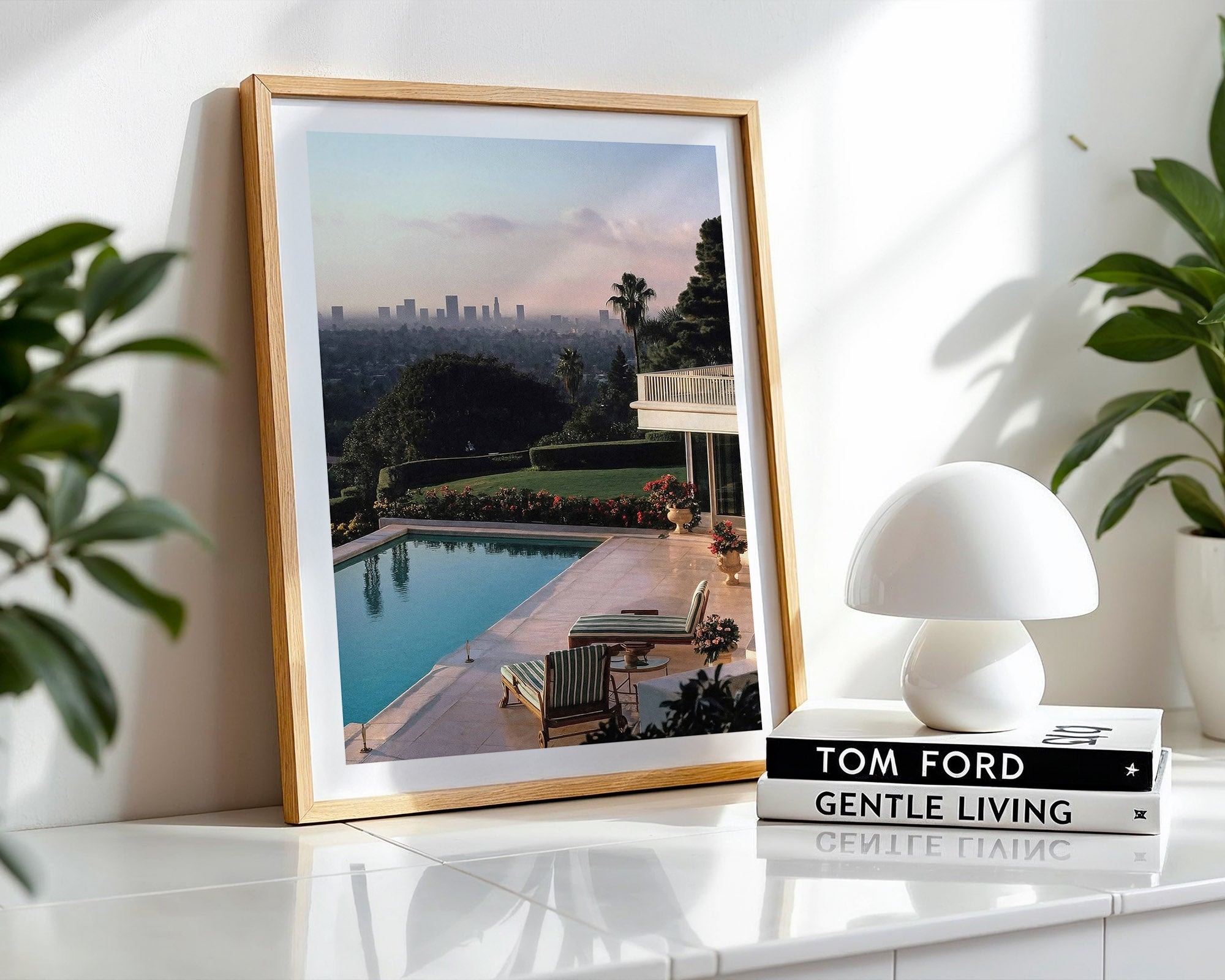 Framed picture of a pool and cityscape Los Angeles on a white surface with a white lamp and books.