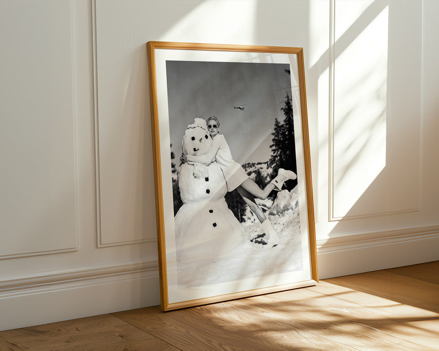 Framed black and white photograph of a person with a snowman against a light wall.